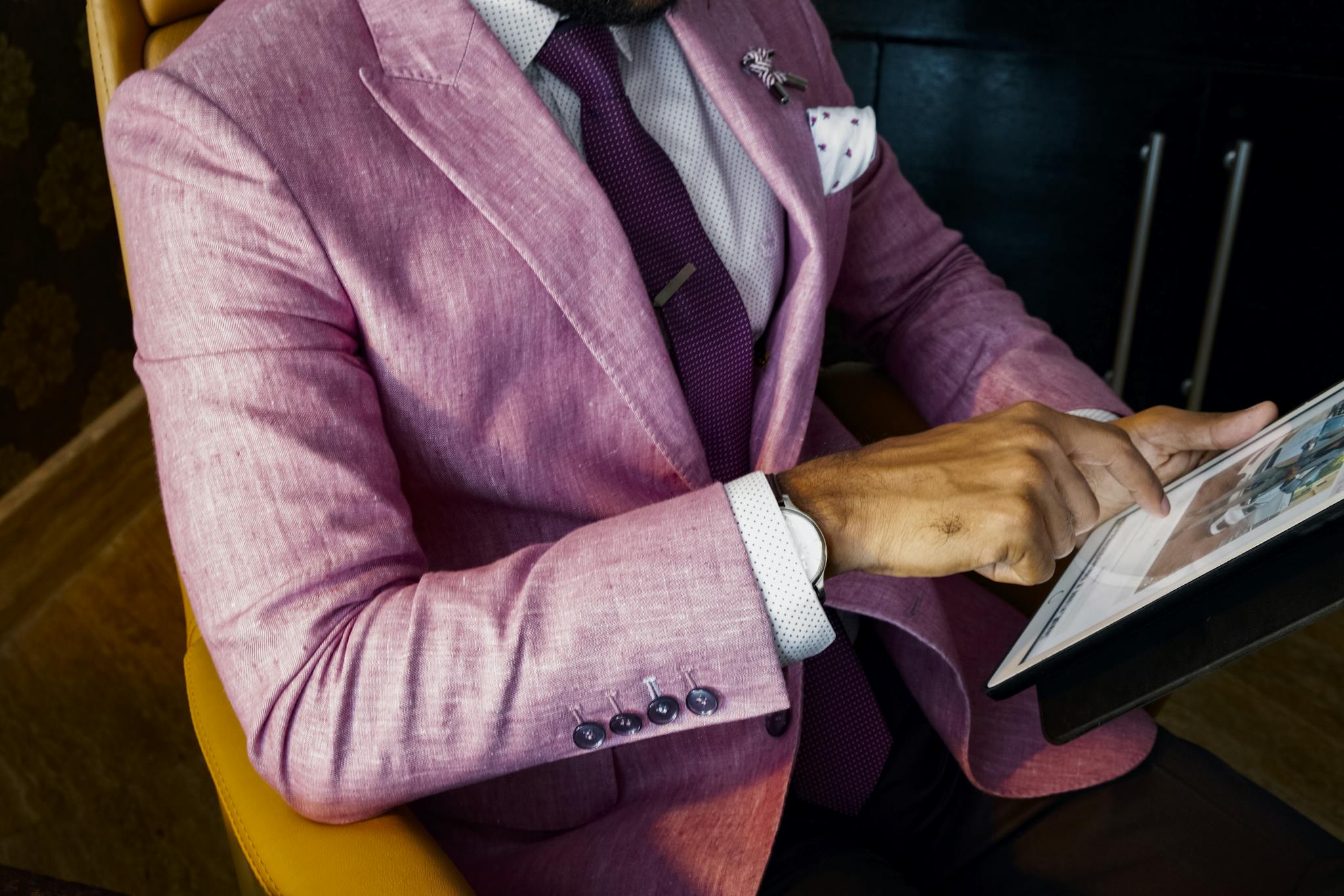 A fashionable businessman in a pink suit uses a tablet in a modern office setting.
