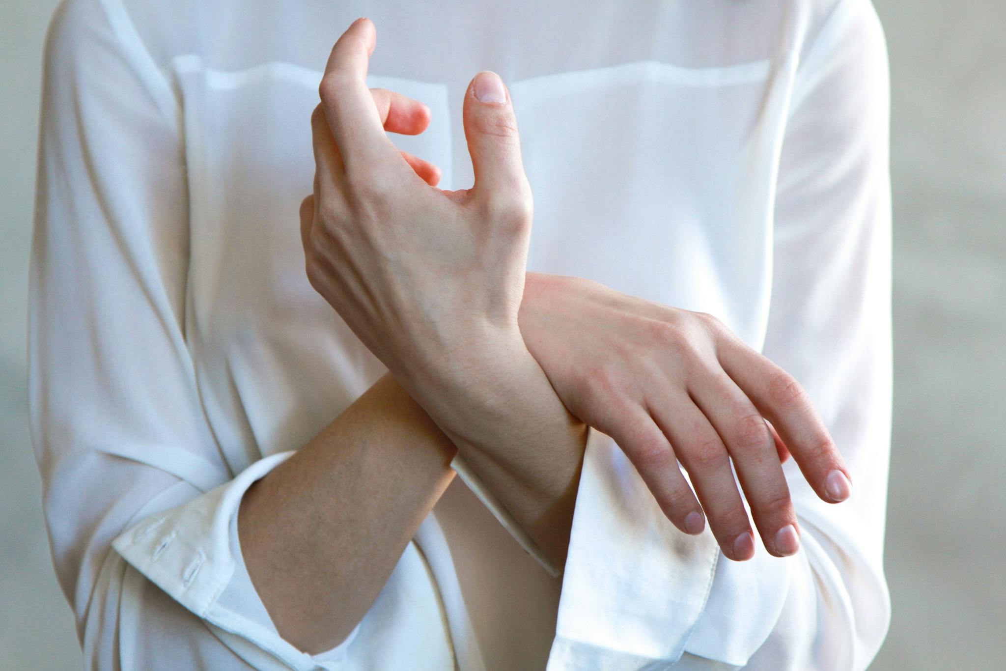 Elegant hands in a white shirt gently touching each other, symbolizing calm and tenderness.