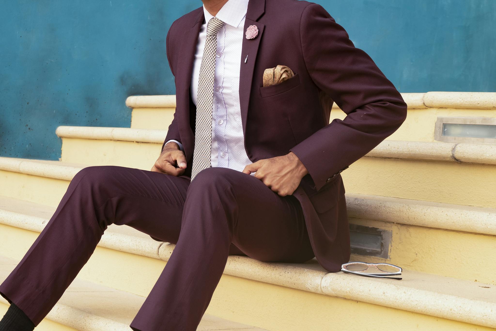 Elegant man in a burgundy suit sitting on steps, exuding sophistication and style.