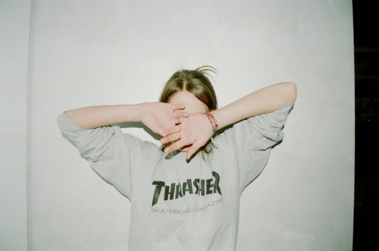 Person wearing a Thrasher sweatshirt covering face, casual and relaxed style.