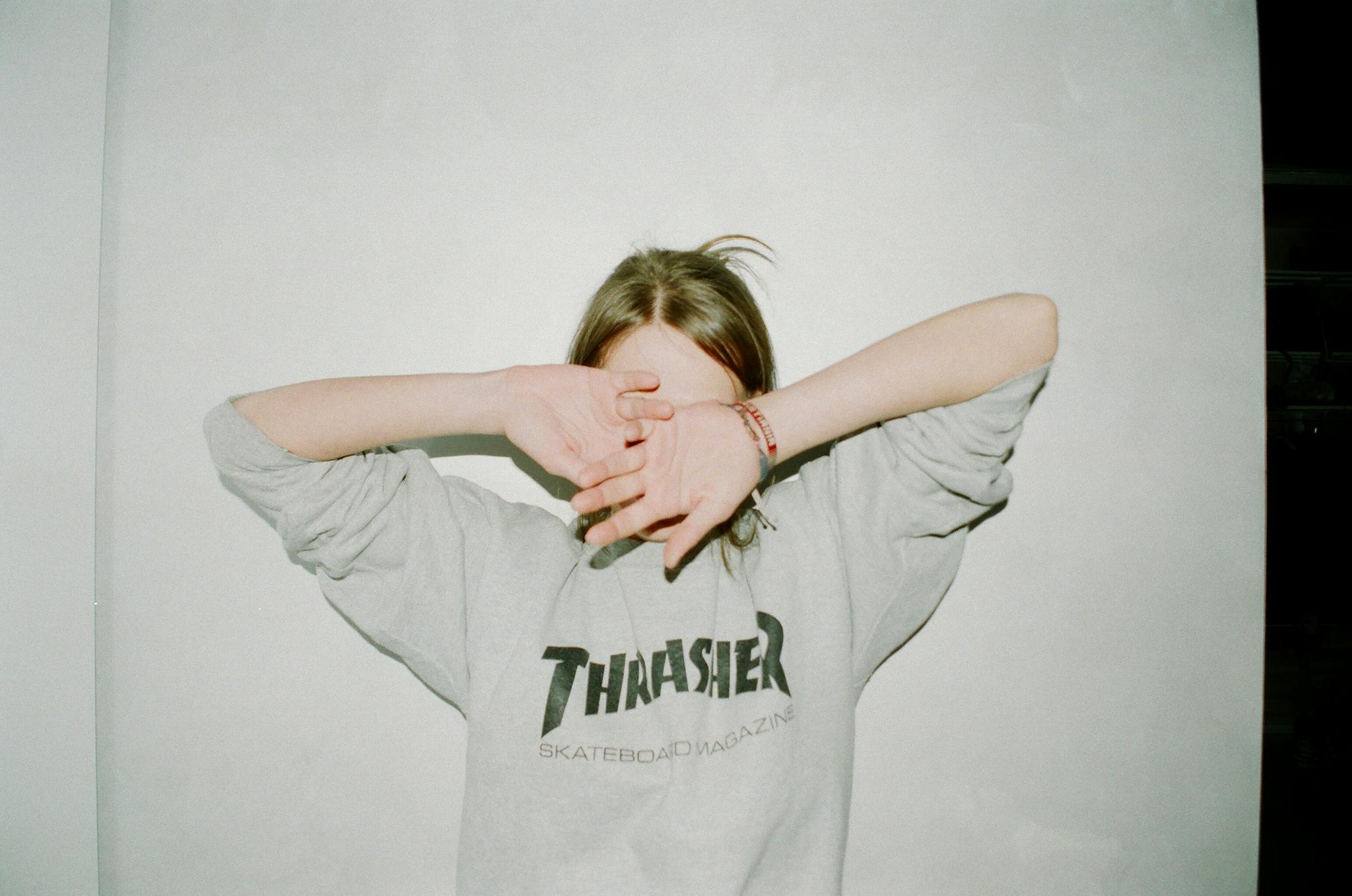 Person wearing a Thrasher sweatshirt covering face, casual and relaxed style.