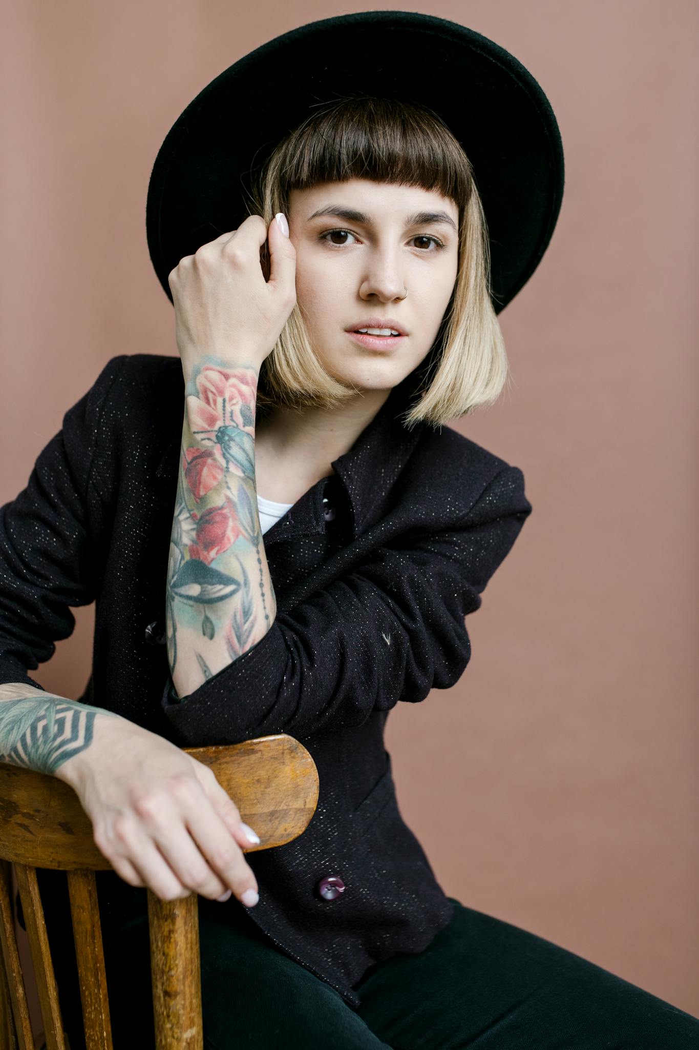 Stylish young woman in hat and tattoos posing indoors with a confident look.